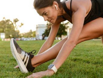 Close up portrait of a fitness woman in earphones doing stretching exercises on grass outdoors