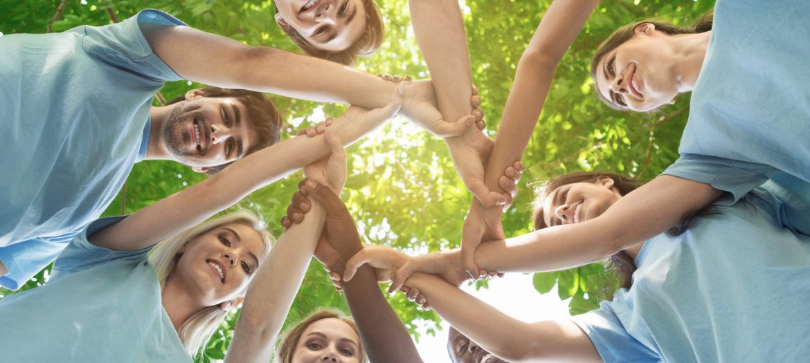 Support concept. Happy volunteers holding hands in circle and smiling, teambuilding exercise, teamwork and help, view from below, copy space